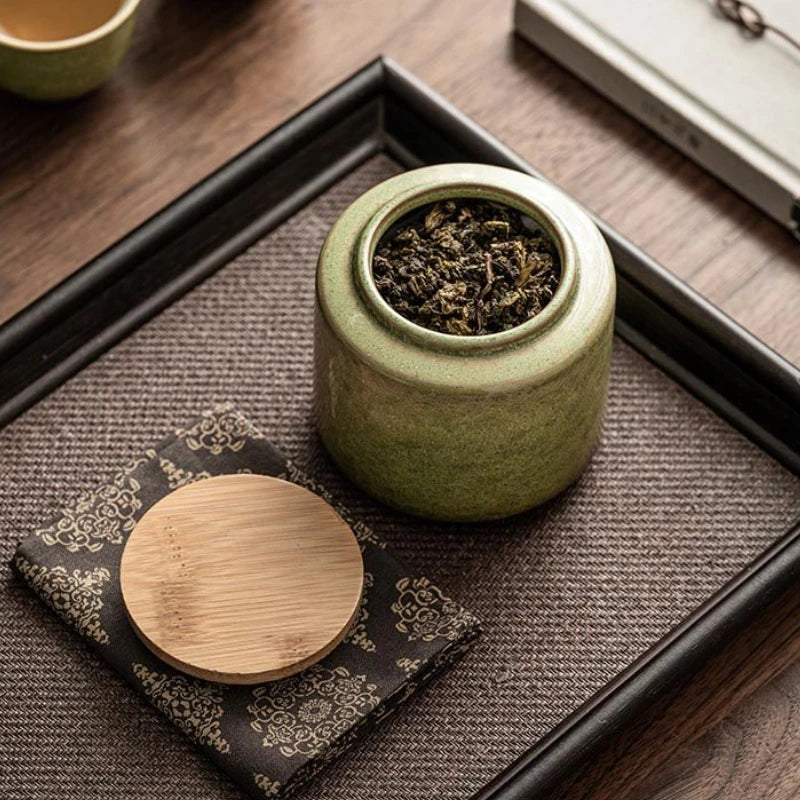 Boîte à thé japonaise ouverte remplie de feuilles de thé, couvercle en bambou posé sur tissu