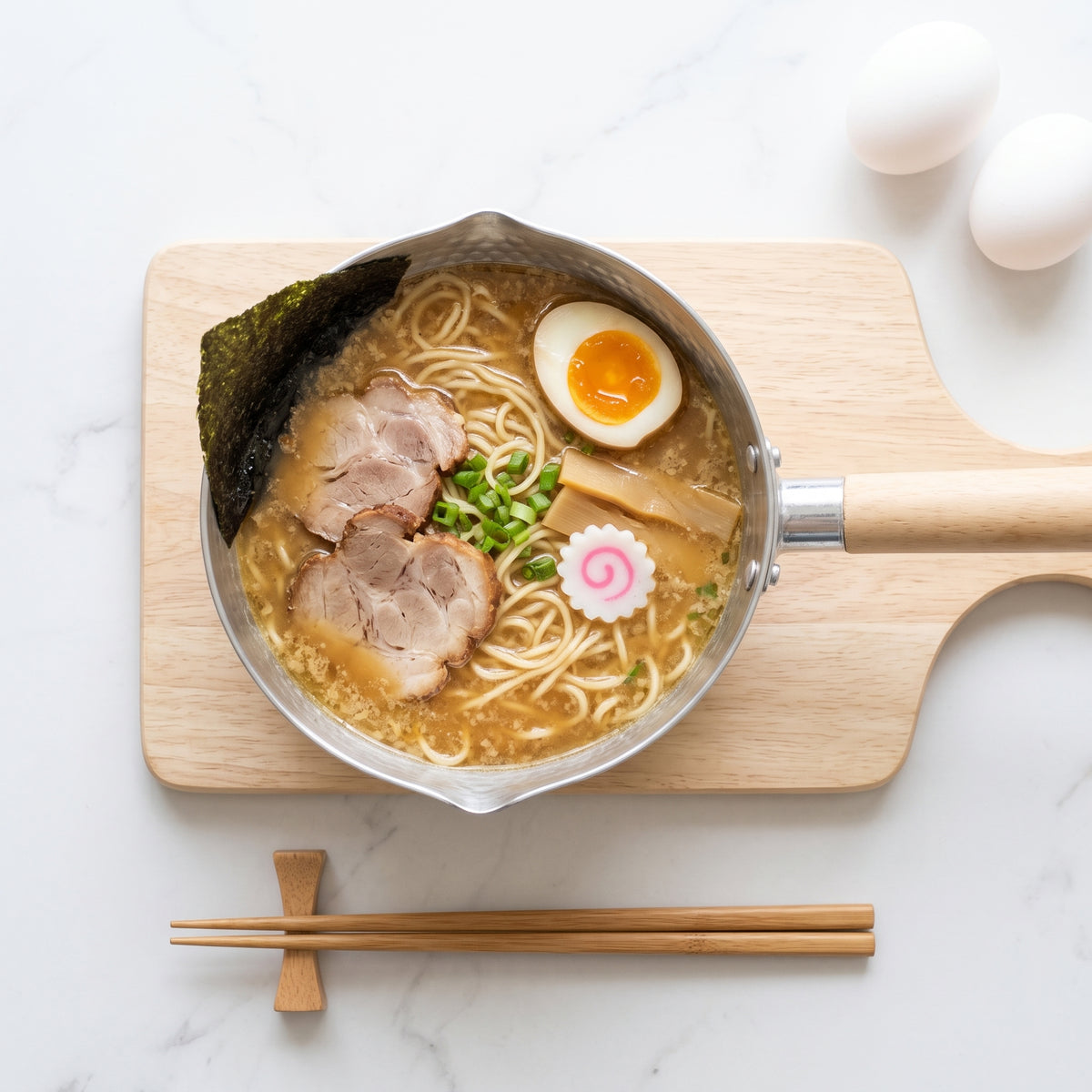 Ramen servi dans la casserole japonaise yukihira, chashu et œuf mollet, baguettes posées sur un repose-baguettes