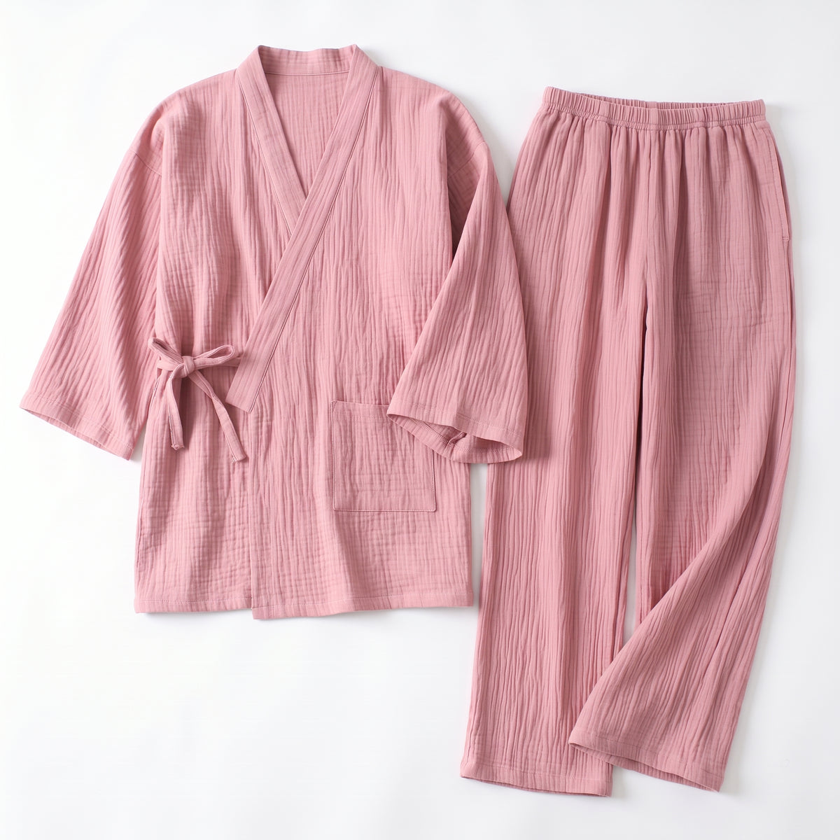 Pyjama japonais rose en gaze de coton froissée, haut croisé noué et pantalon, posés à plat sur fond clair