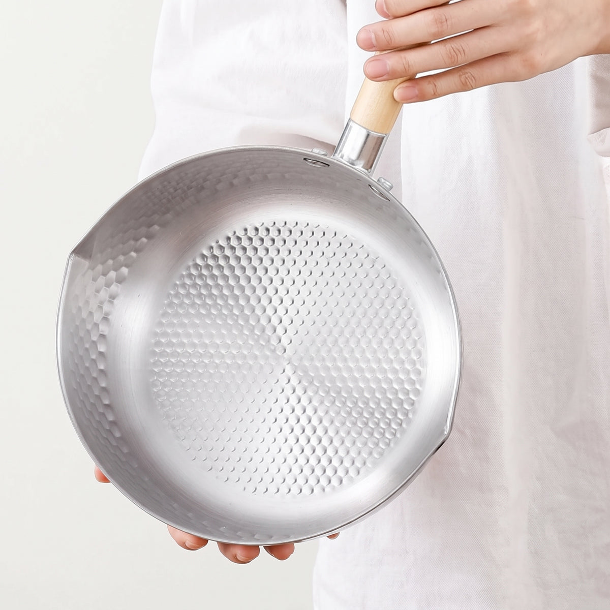 Casserole japonaise yukihira tenue à la main, l'intérieur martelé de petites facettes jusqu'au fond