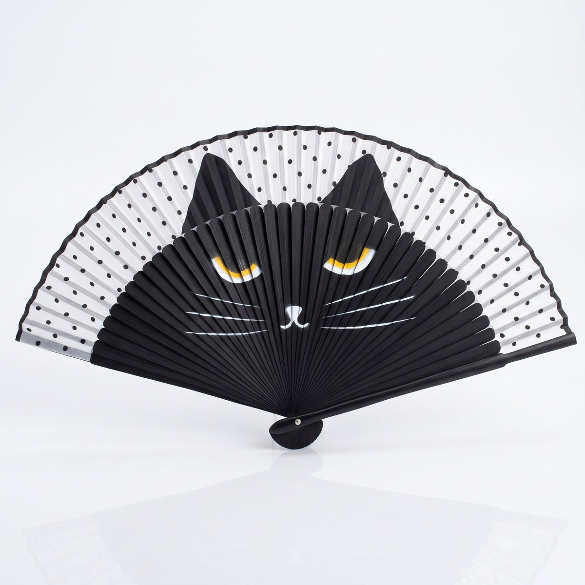 Éventail japonais chat noir ouvert, yeux jaunes et moustaches blanches sous une feuille blanche à pois noirs