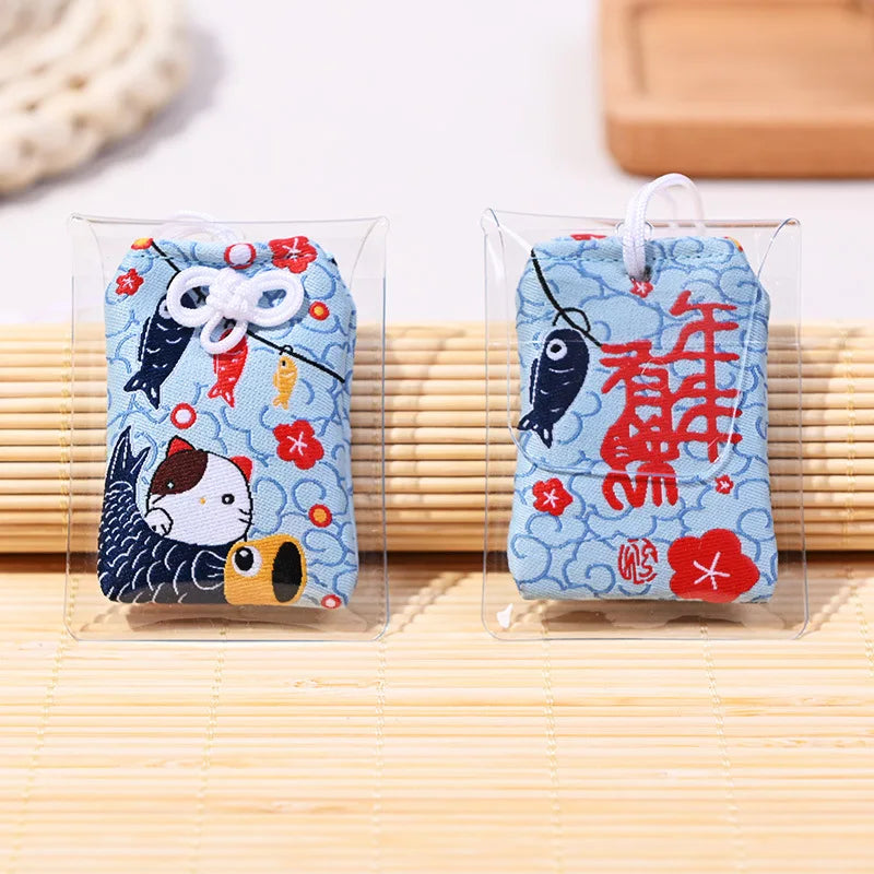 Omamori japonais bleu ciel brodé avec Maneki-Neko et Koinobori pour la croissance et l'abondance familiale.