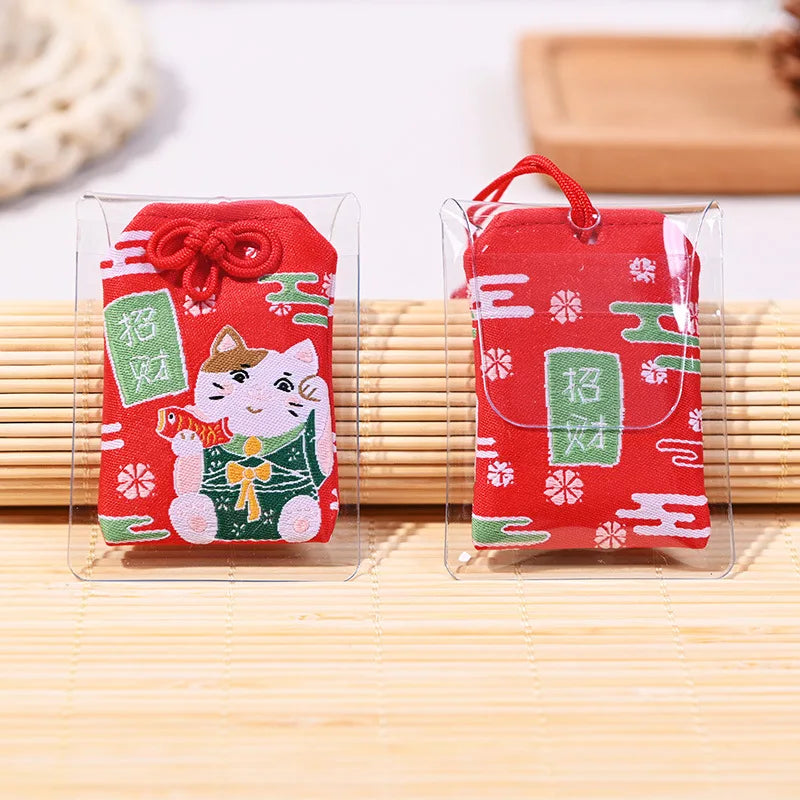 Omamori rouge japonais brodé avec Maneki-Neko tenant un poisson Tai pour inviter la fortune et célébrer le succès.