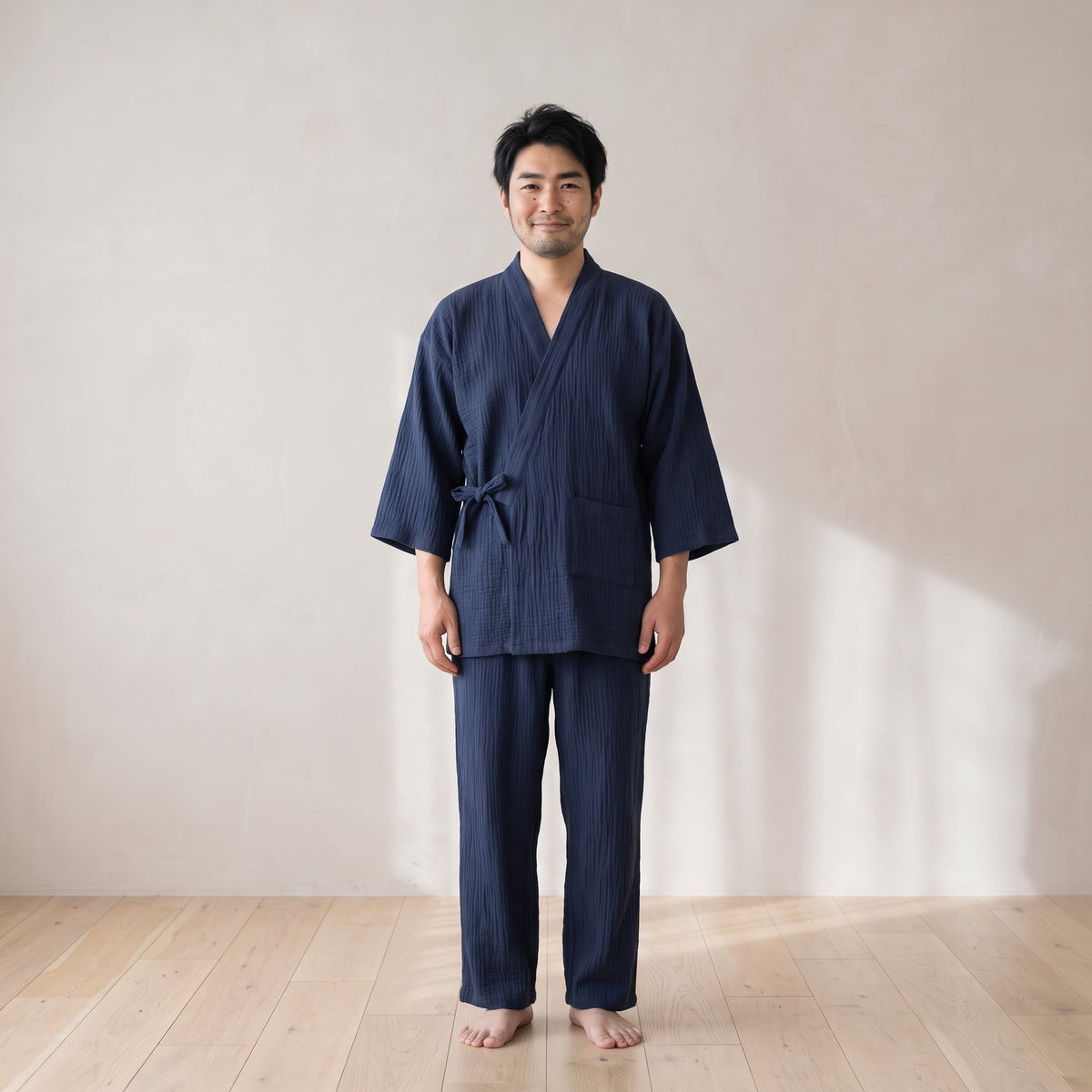 Homme debout pieds nus portant le pyjama japonais bleu marine, haut croisé noué à la taille