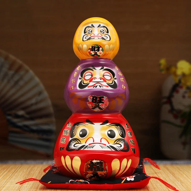 Tirelire totem japonaise composée de trois Darumas empilés de couleurs rouge violet et jaune en céramique.